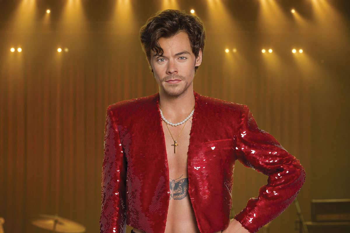 A wax figure of Harry Styles in a red sequin jacket, chest tattoo and necklaces visible underneath.