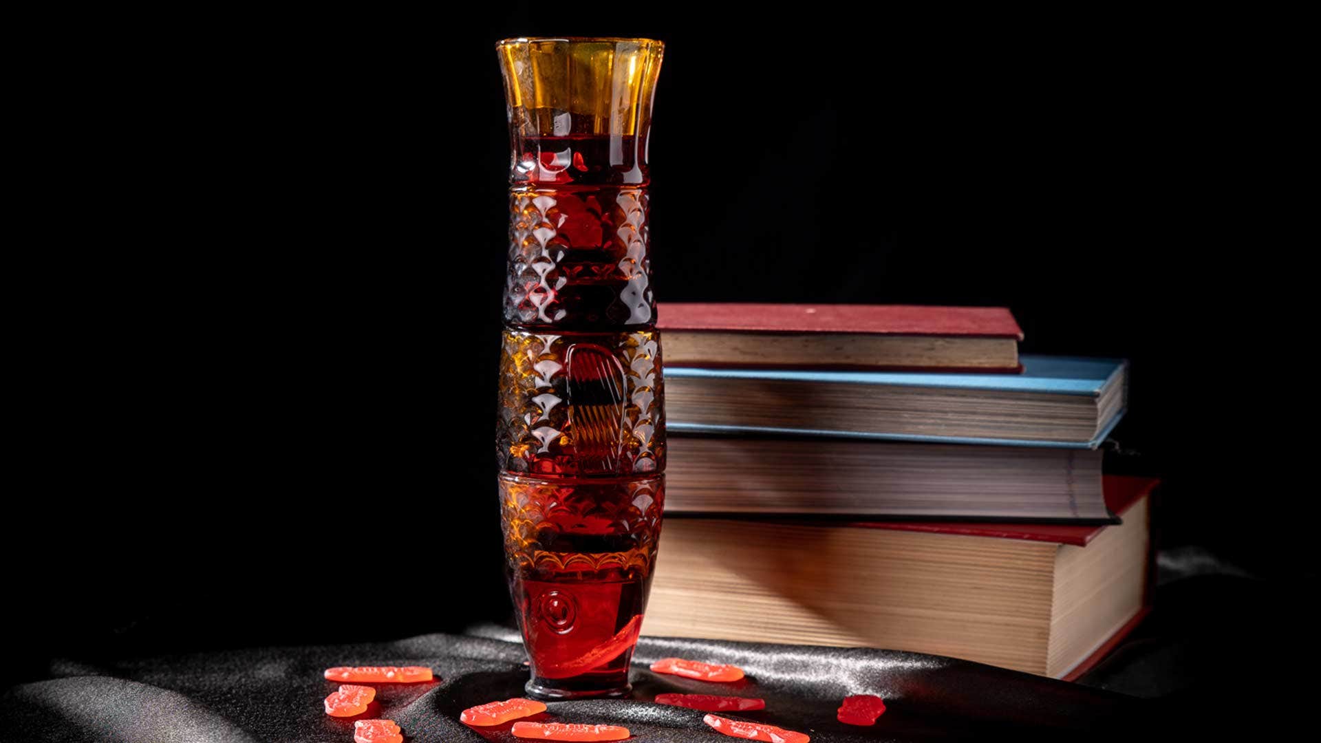 A tall, colorful vase stacked with books in the background and scattered red candies on a dark surface.