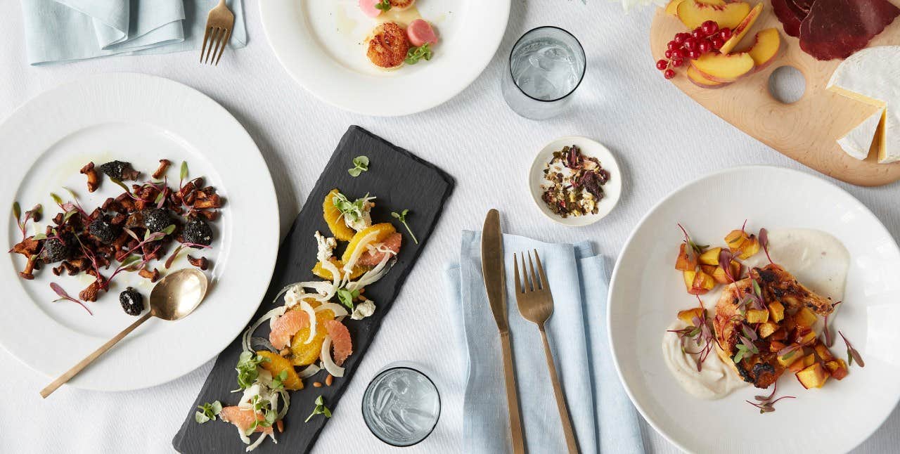 A table set with various gourmet dishes, including salads and appetizers, with cutlery and glasses on a white tablecloth.