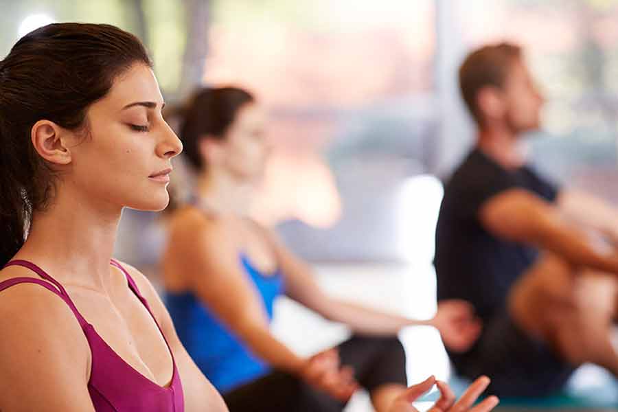 Three people meditating in a yoga class, sitting cross-legged with eyes closed, focusing on their mindfulness practice.