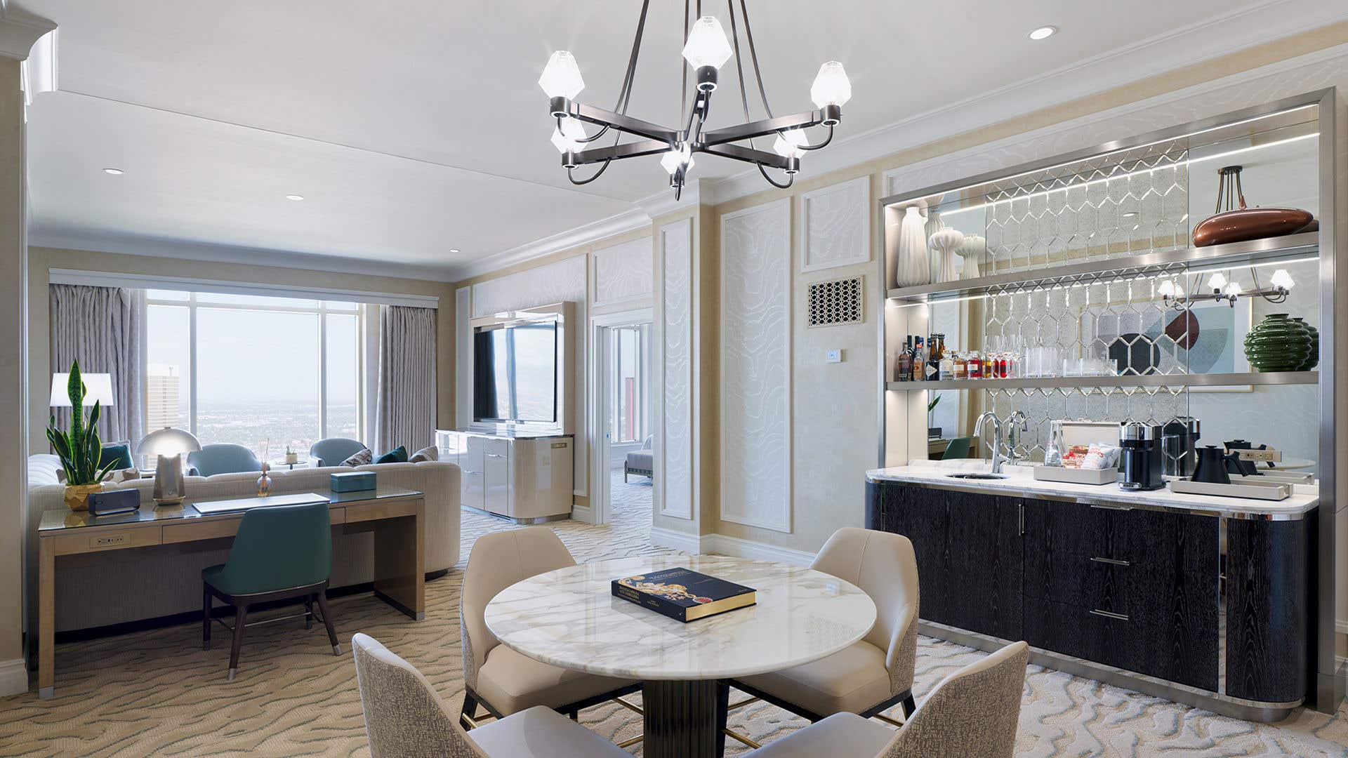 A living room in soft color palette with a bar, dining table, desk, and couch.