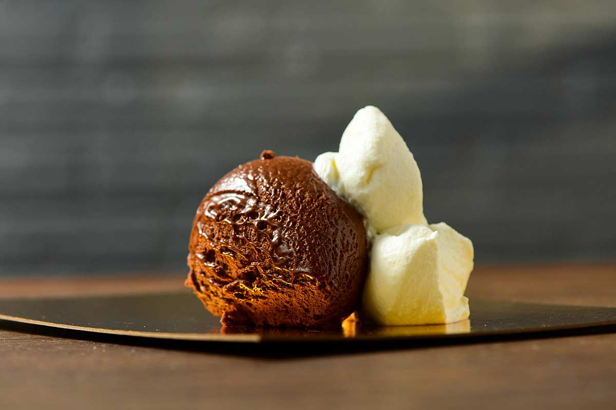 A scoop of chocolate ice cream and two dollops of whipped cream on a reflective surface.